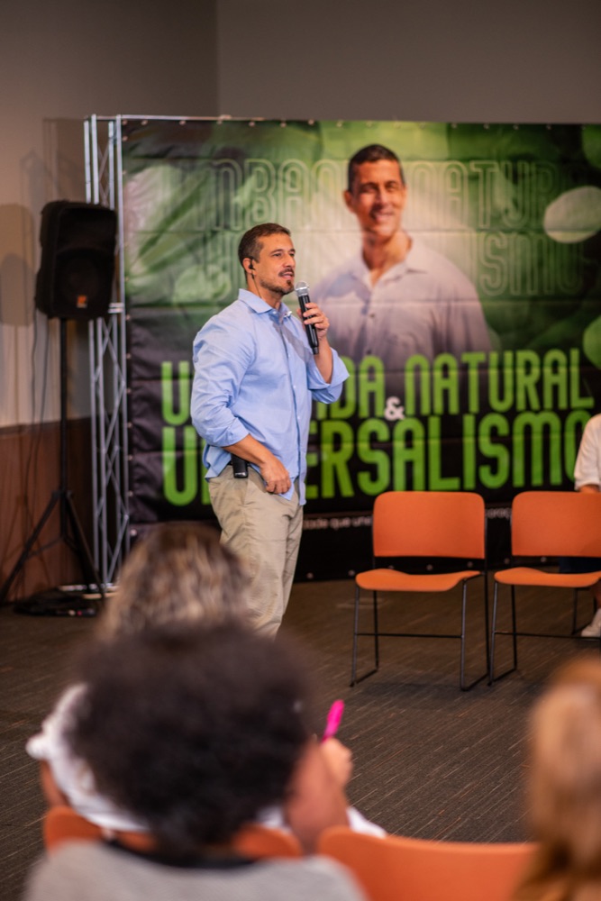 Ricardo Di Napoli falando ao microfone, banner Umbanda Natural & Universalismo ao fundo